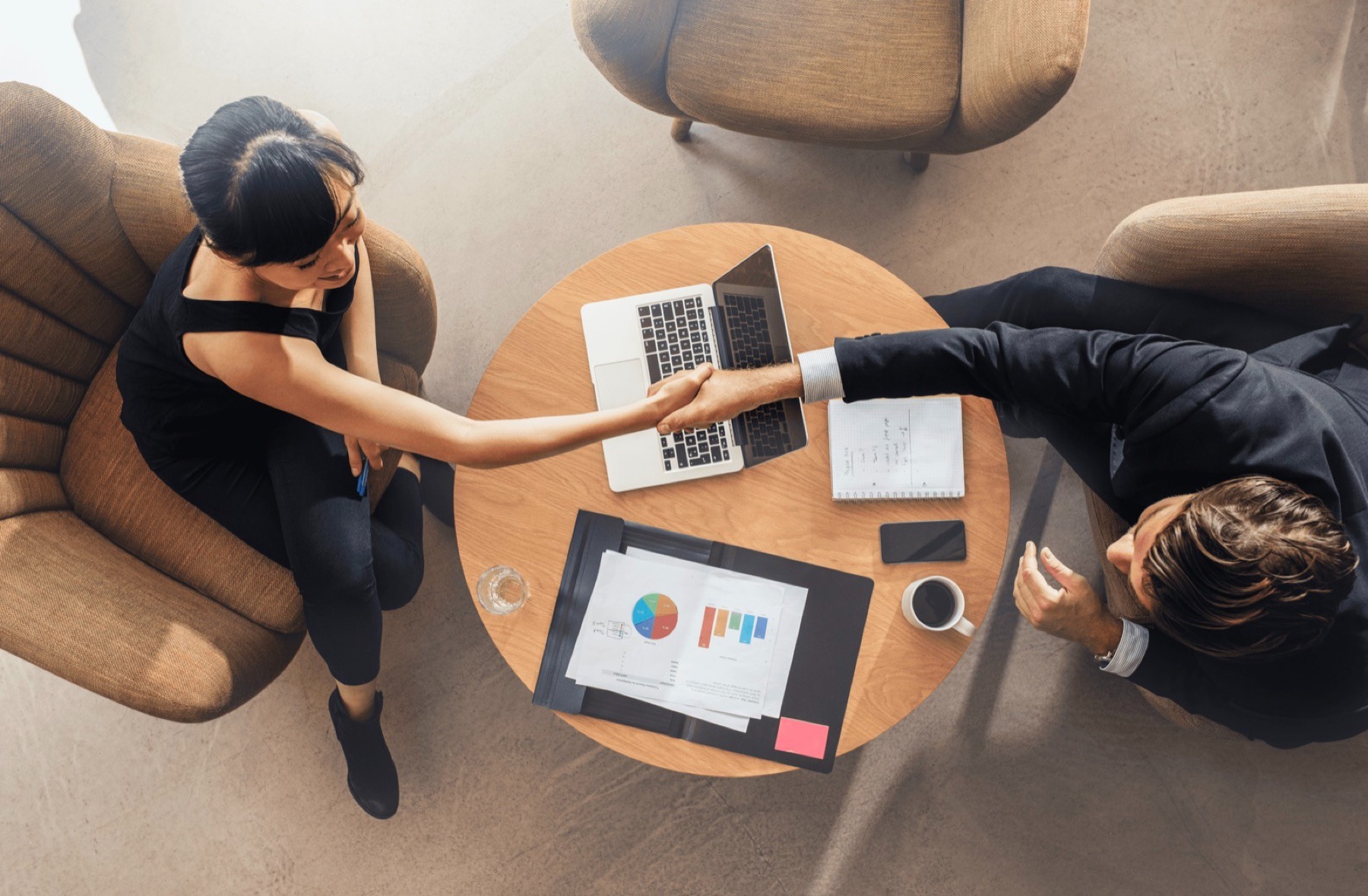 Handshake over a table with charts and a laptop